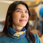 A woman wearing a neck gaiter with an orang, yellow and blue design featuring a clown fish.