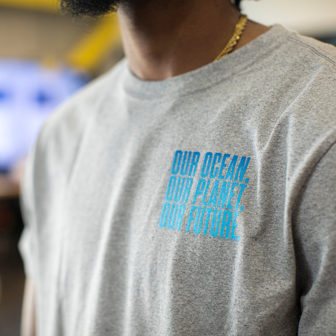 Close up of the logo on the front left chest of heather gray t-shirt that says, Our Ocean, Our Planet, Our Future.  Logo is different shades of blue.