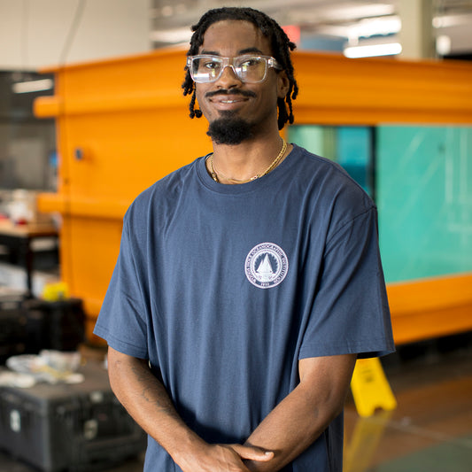 Man wearing a navy blue t-shirt with the WHOI Classic Seal Logo on the front left chest.