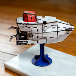 A close-up of a 3D model of the deep-sea submersible Alvin on a blue display stand. The background shows a blurred instruction booklet on a wooden table.